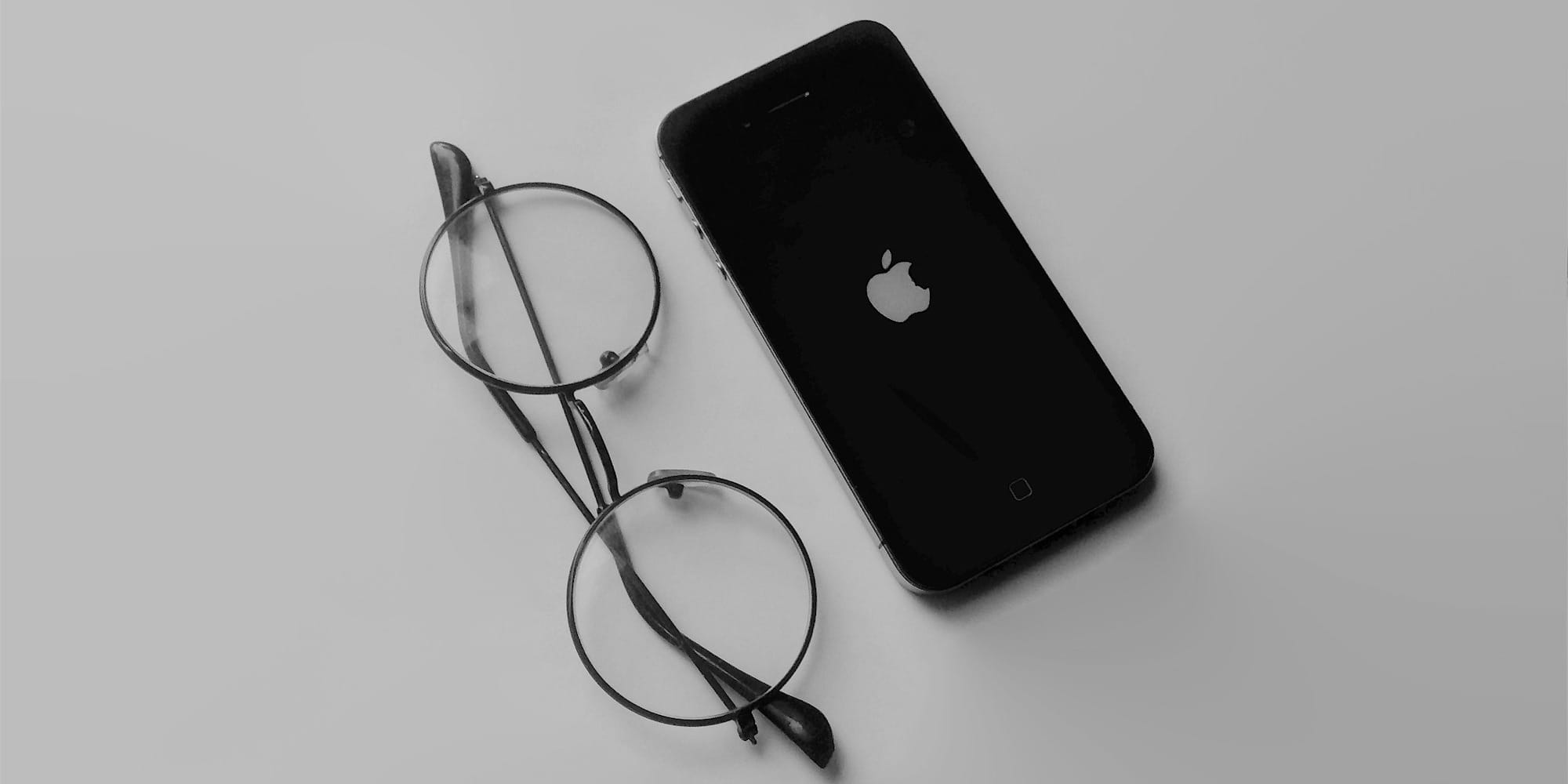 black iphone 4 beside black framed eyeglasses